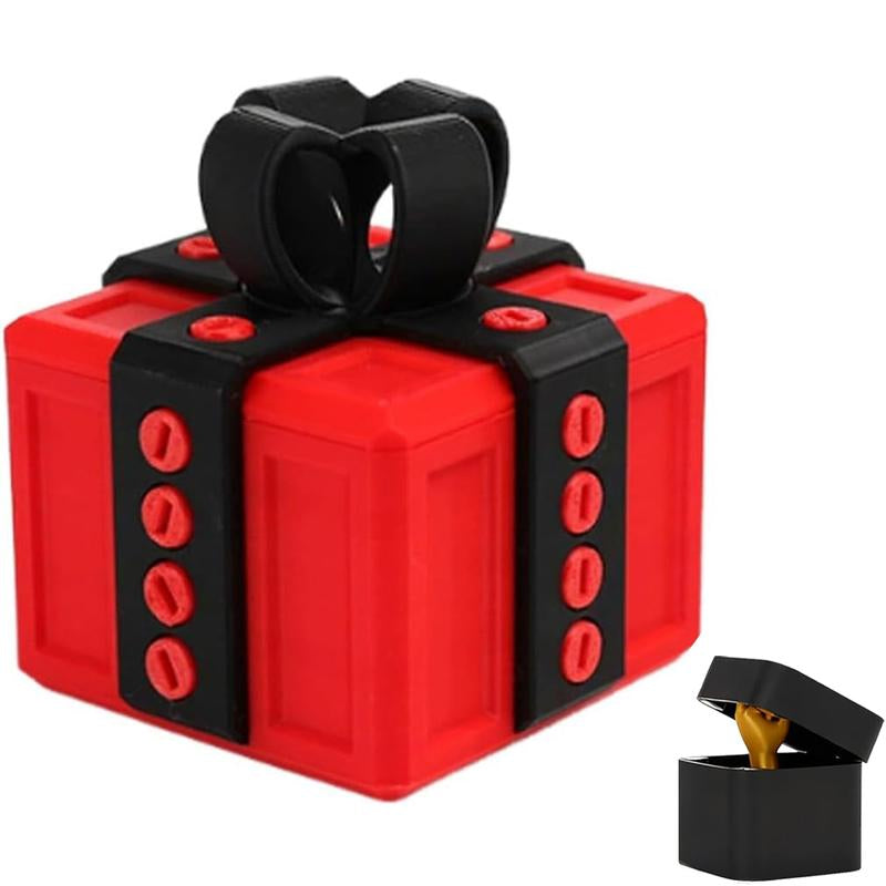 Red gift box with black straps and bow resembling Lego bricks beside a small black ring box with a gold ring inside